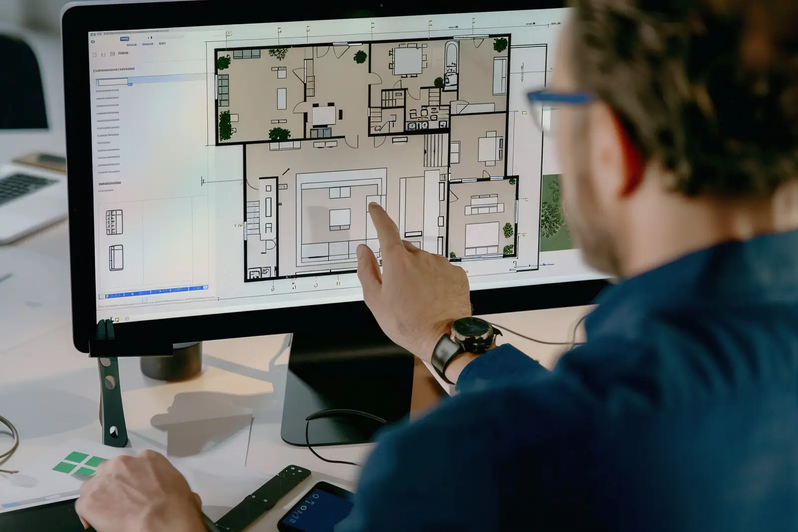 A hand pointing to a home floor plan on a computer monitor