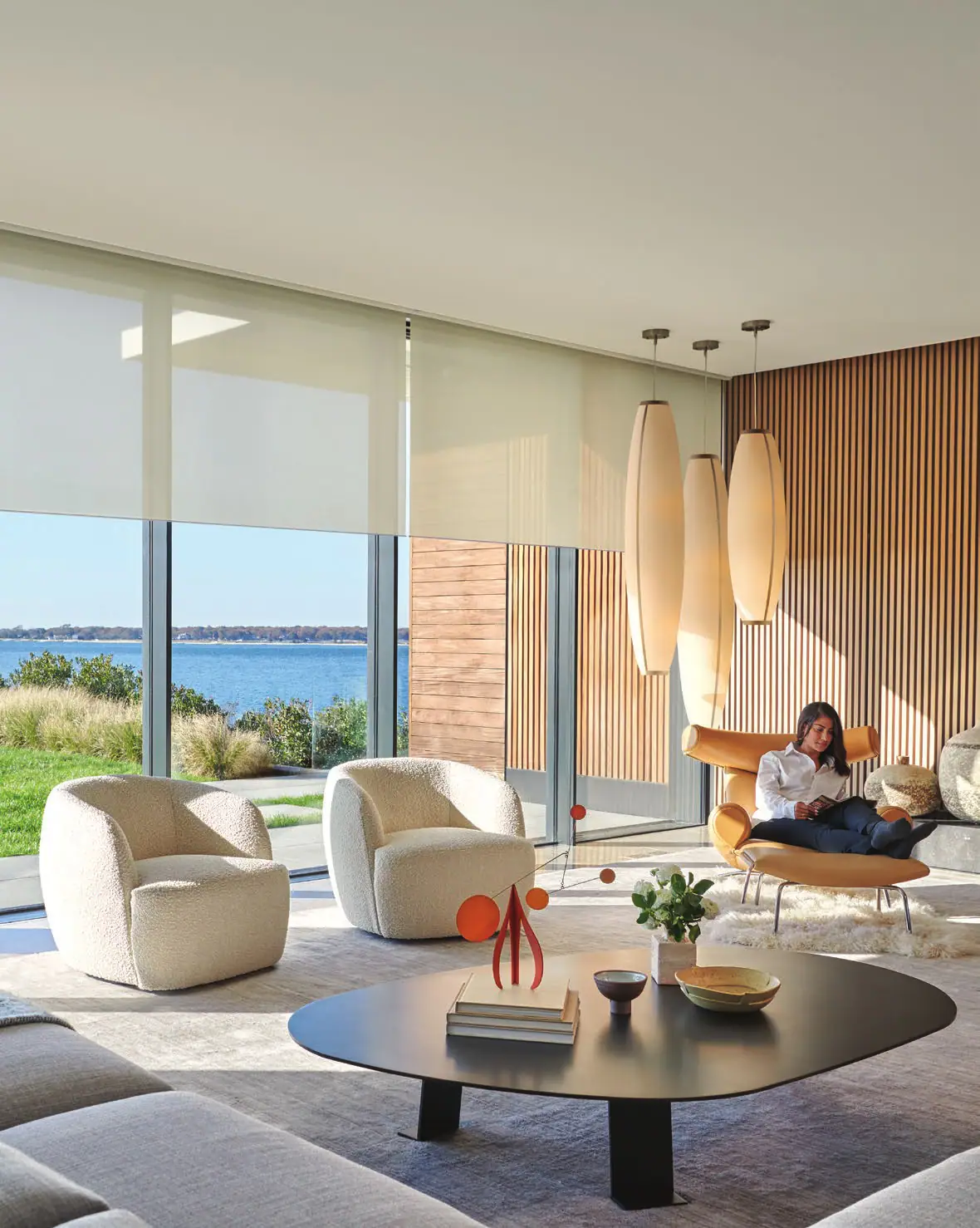 A waterfront living room with Lutron roller shades raised over walls of glass